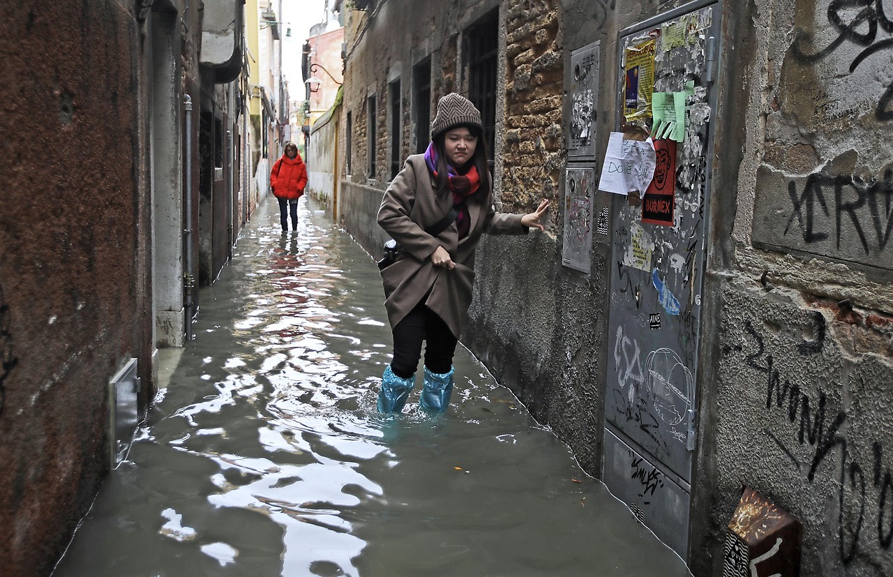 Touristin stapft in Gummistiefel durch die überfluteten Gassen von Venedig