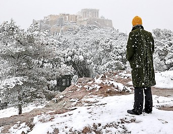 Ein Mann blickt in der griechischen Hauptstadt Athen auf die schneebedeckte Akropolis