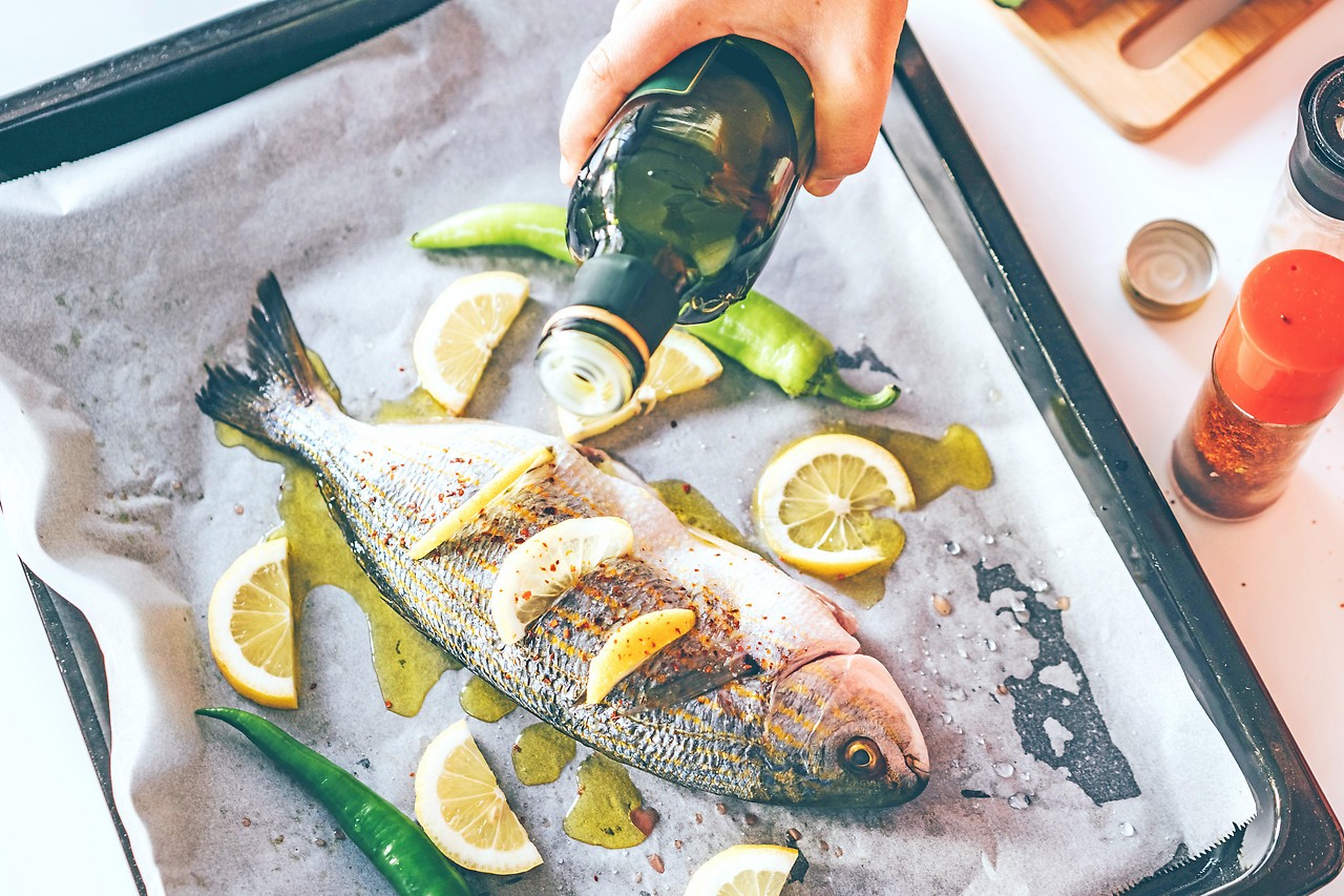 Un pescado en una bandeja para hornear está adornado con aceite de oliva.