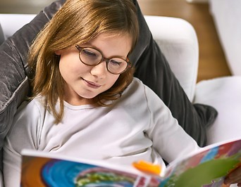 Junges Mädchen mit Brille liest in einem Buch