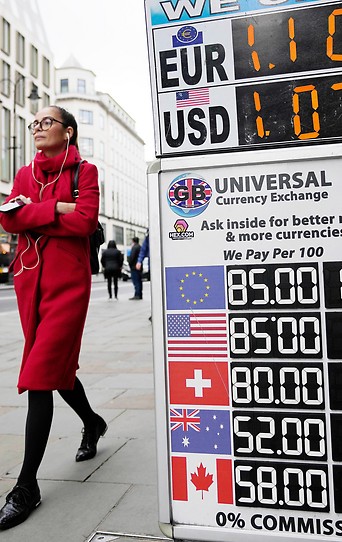 Eine Frau geht in London an einer Wechselstube mit Wechselkurswerten vorbei