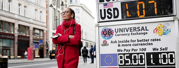 Eine Frau geht in London an einer Wechselstube mit Wechselkurswerten vorbei