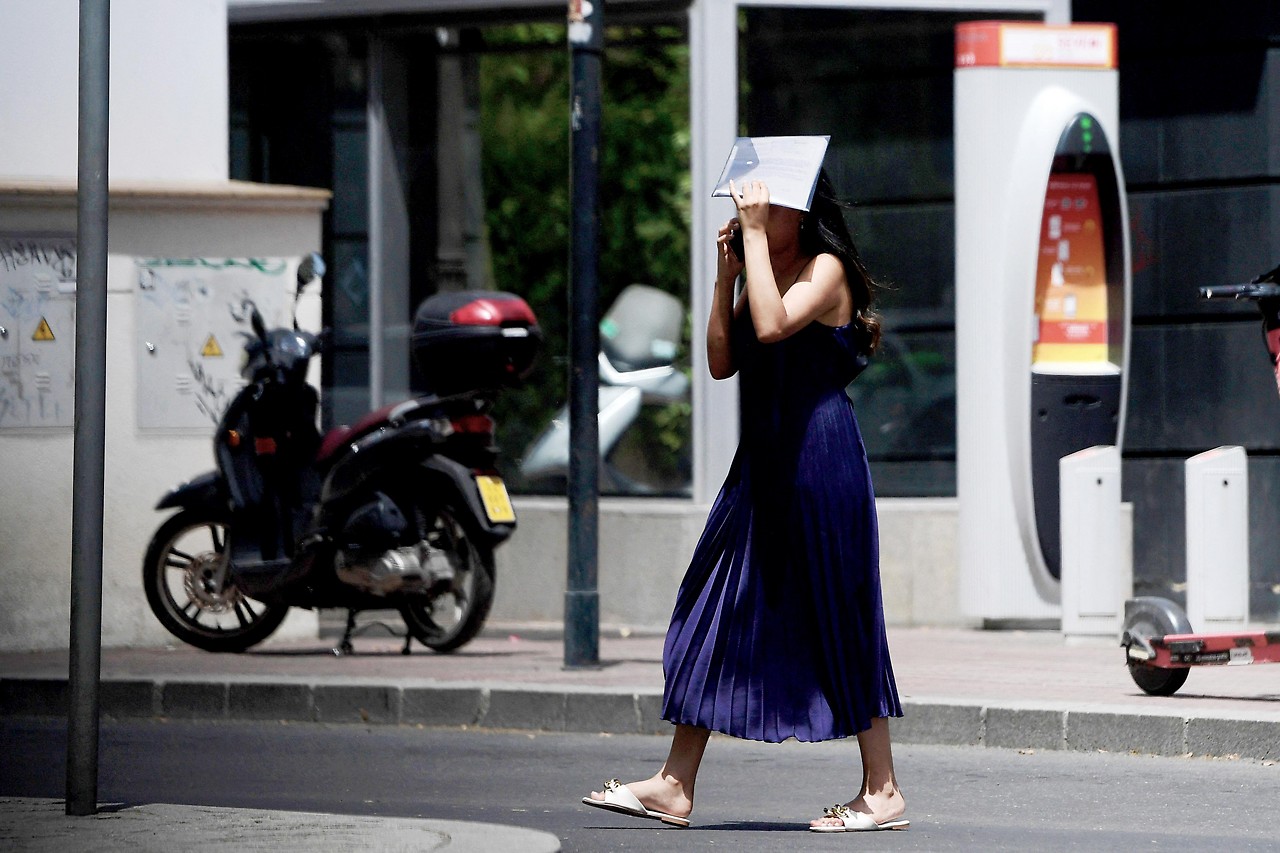 A passer-by shields her head with a newspaper in Seville