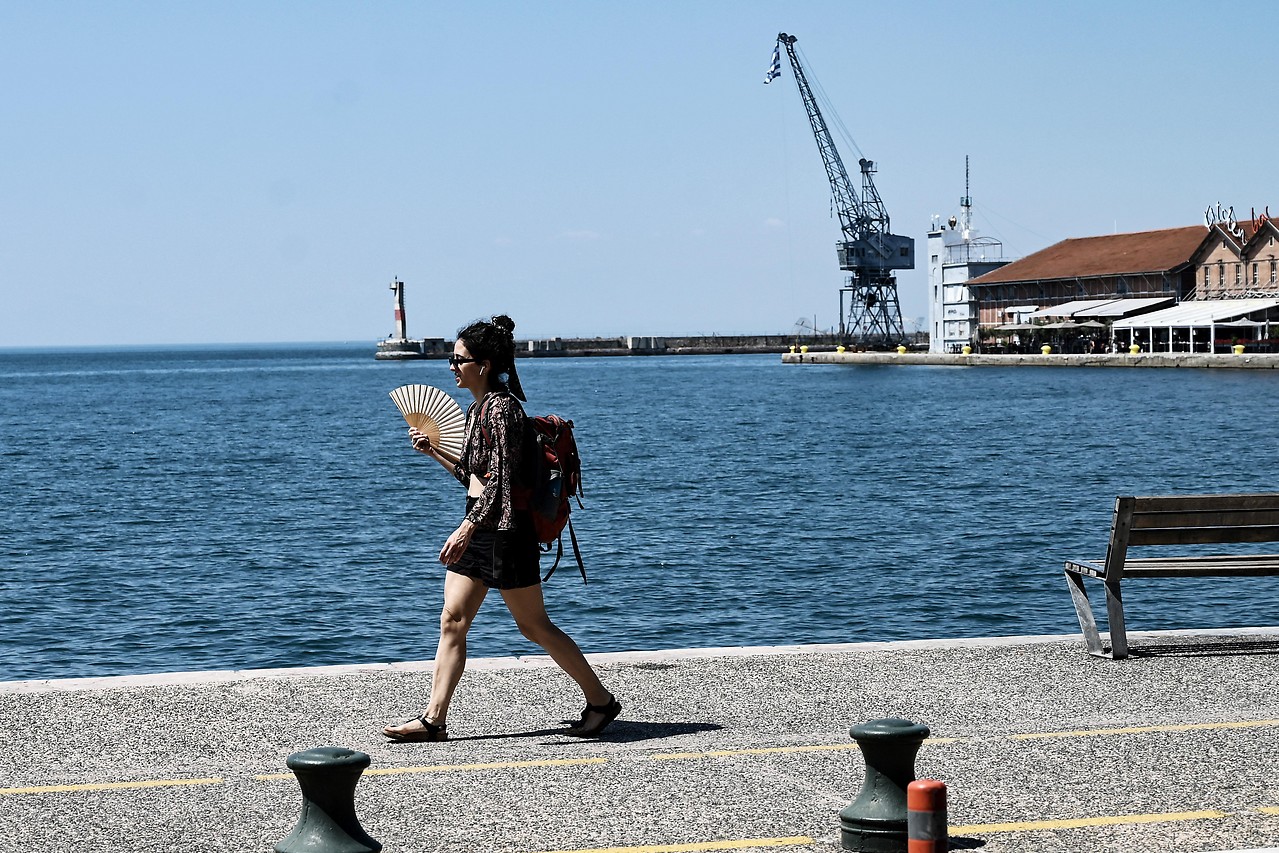 A passer-by walks through the port of Thessaloniki with a fan in her hand