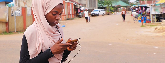Junges Mädchen in Afrika schaut auf ihr Handy während sie auf der Straße geht