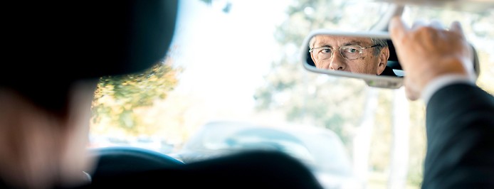 Älterer Mann blickt in den Rückspiegel seines Autos