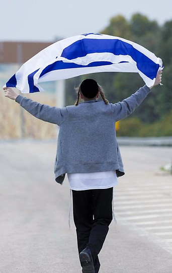 Ein religiöser Jude mit Israel-Flagge vor einer Straßenblockade der israelischen Armee