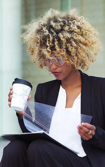 Frau liest mit Kaffeebecher in der Hand in Unterlagen