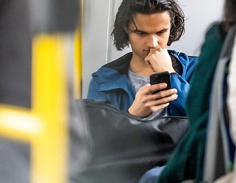 Junger Mann liest im Bus am Smartphone