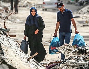 Palästinenser mit befüllten Säcken zwischen zerstörten Gebäuden in Chan Junis 