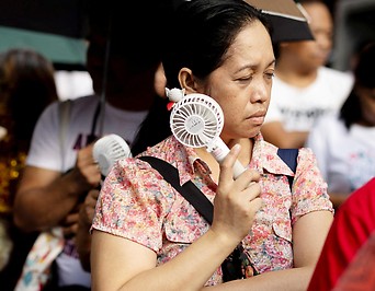 Eine Frau in Manila kühlt ihren Kopf mit einem Mini-Ventilator